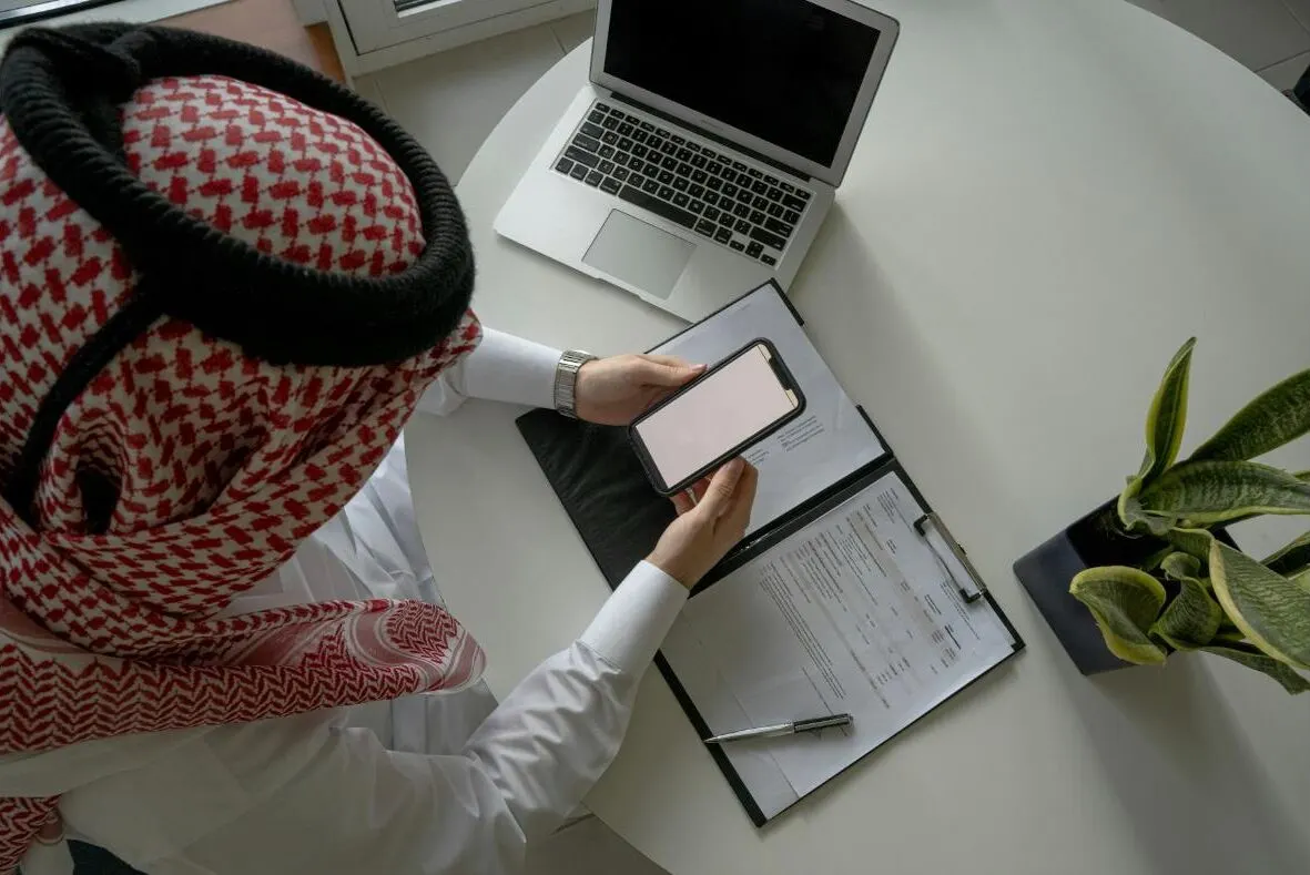 A business owner checking orders on his phone next to a laptop
