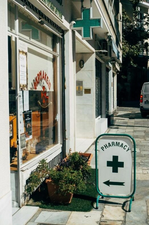 A neighbourhood pharmacy storefront with a pharmacy sign on the pavement