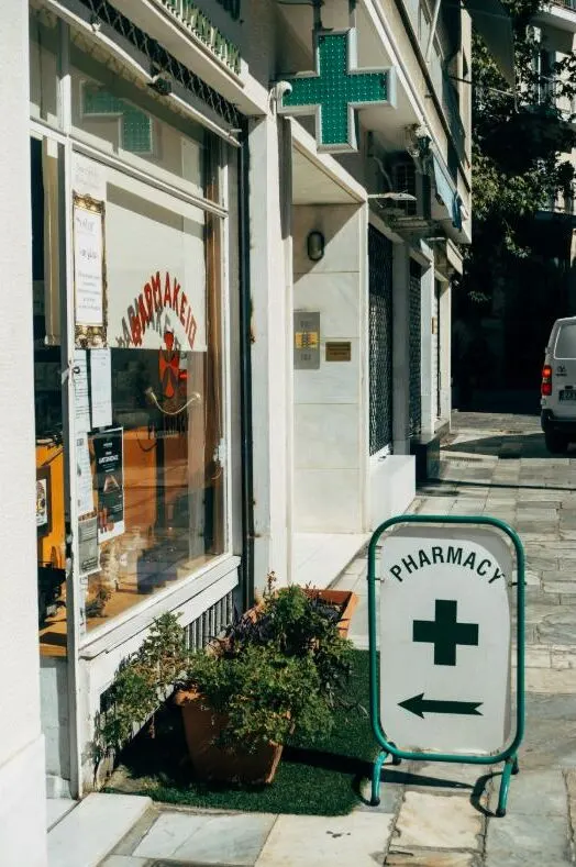 A neighbourhood pharmacy storefront with a pharmacy sign on the pavement